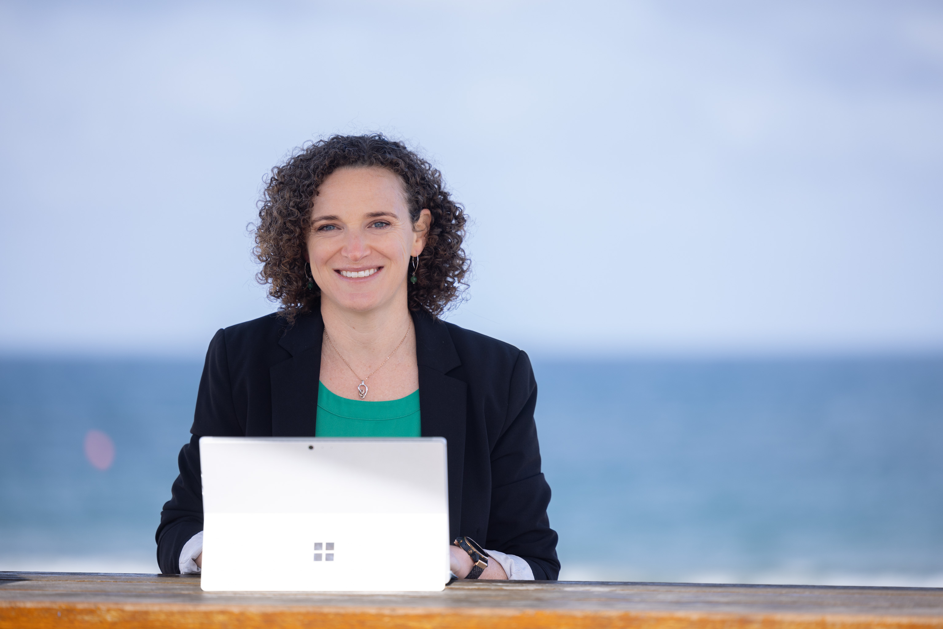 Picture of Ashley Caspers, SEO copywriter, writing on laptop in front of the ocean.